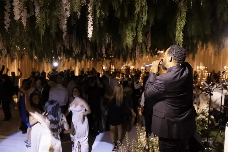 Singer performing at a formal event while guests dance under hanging floral decor.